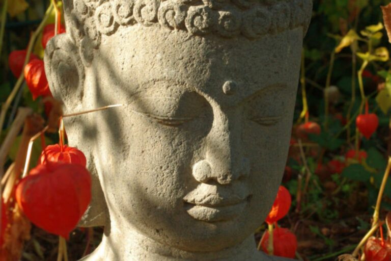 Buddha-Statue im Garten mit roten Laternenblumen